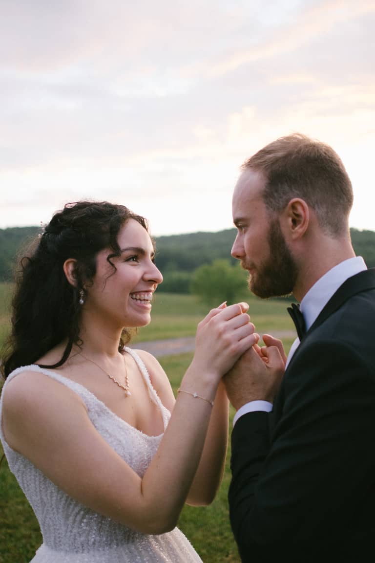 Bride and groom holding hands outdoors at sunset, sharing a joyful moment during their wedding