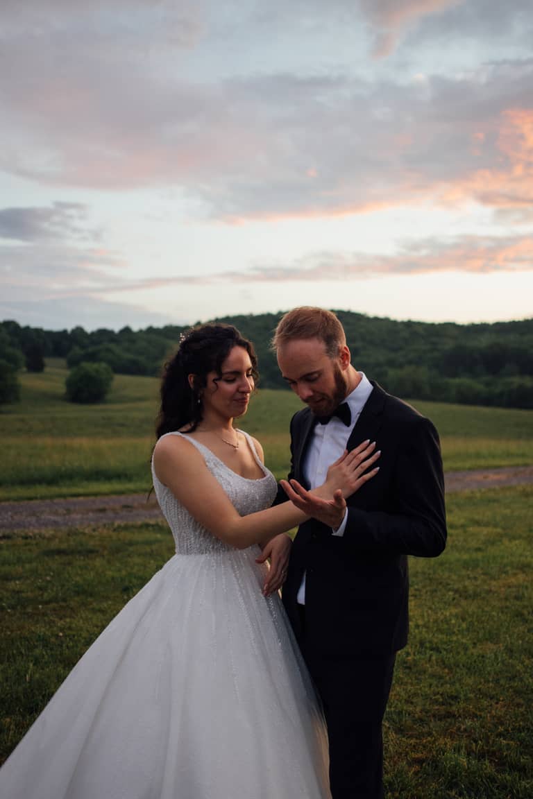 Bride and groom embrace in a grassy field at sunset during their wedding