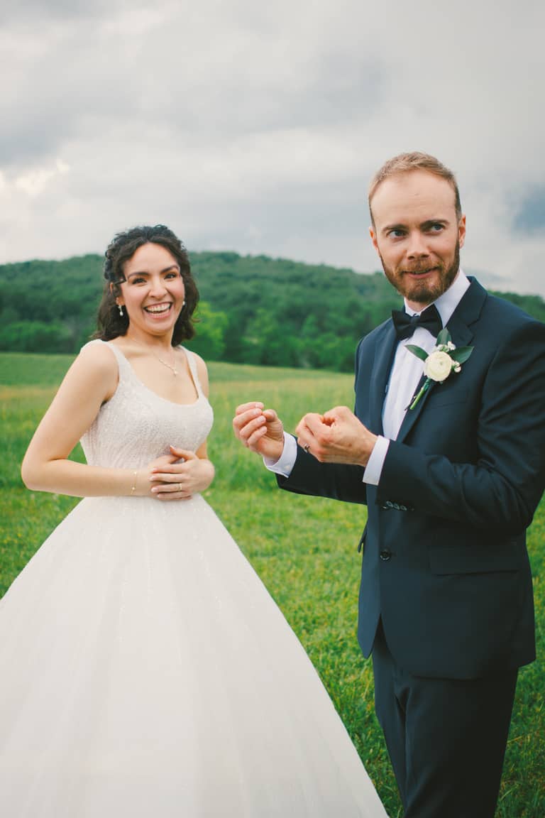 Joyful bride and groom pose in a grassy field with rolling hills behind them