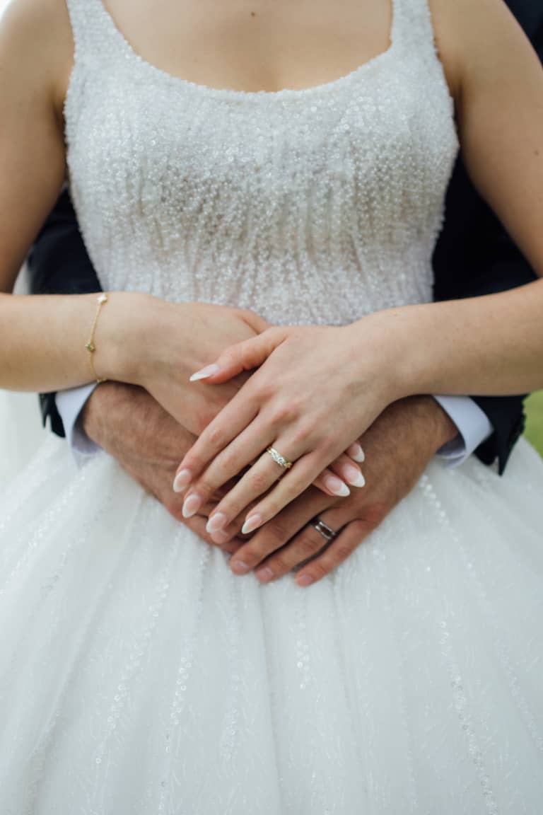 Bride and groom's hands with wedding rings clasped over her dress