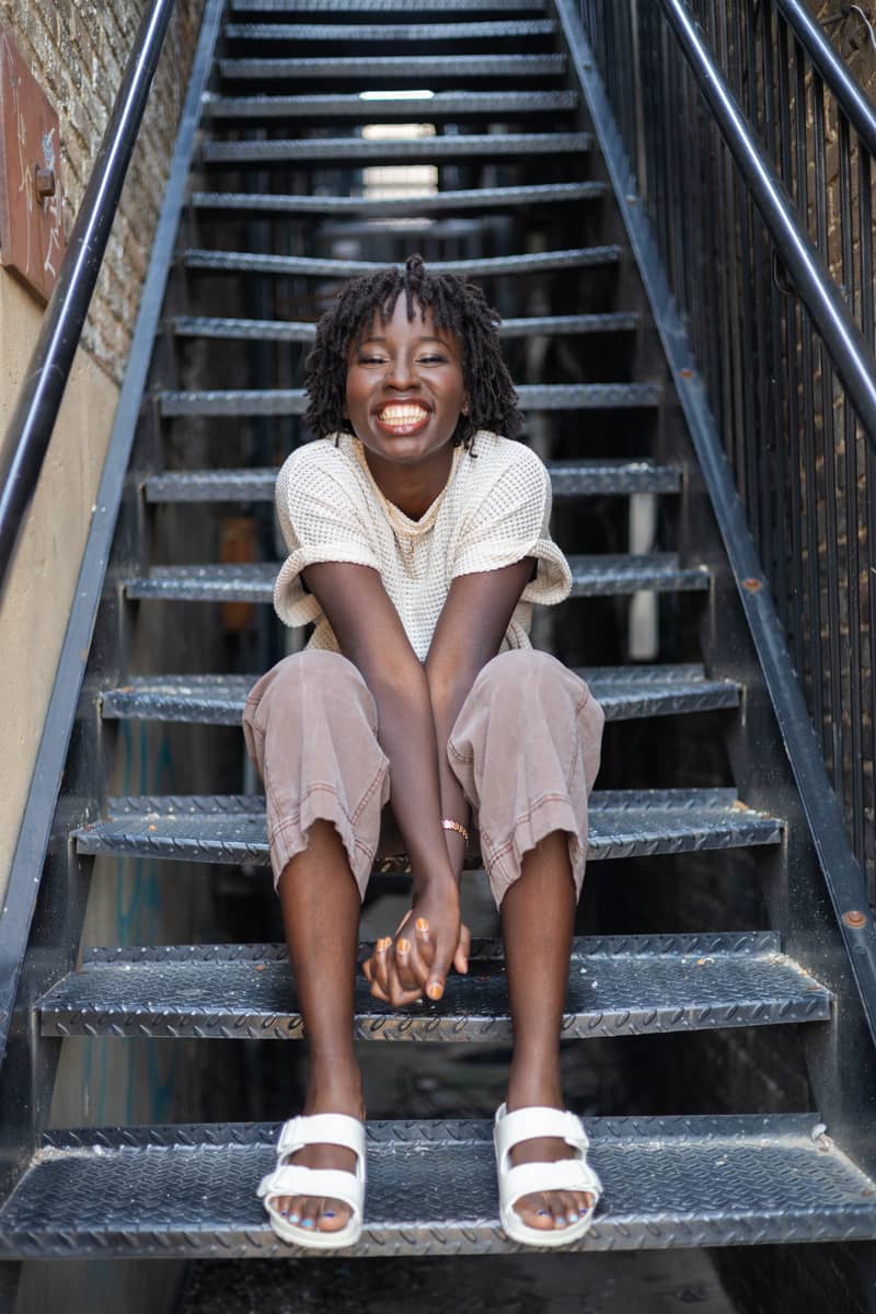 Young woman with dreadlocks laughs joyfully while sitting on outdoor metal stairs