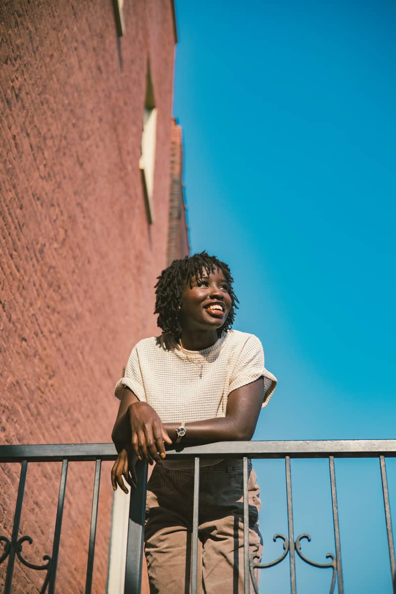 Smiling woman leans on railing against brick building and bright blue sky