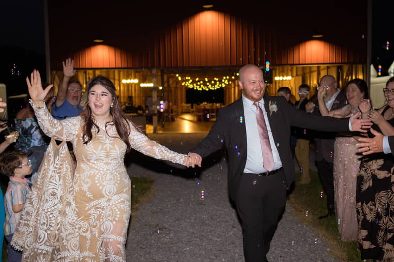 Joyful wedding couple walks through bubbles outside a barn reception venue