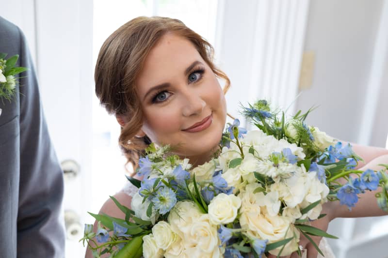 Bride smiles holding a bouquet of white and blue flowers during her wedding day
