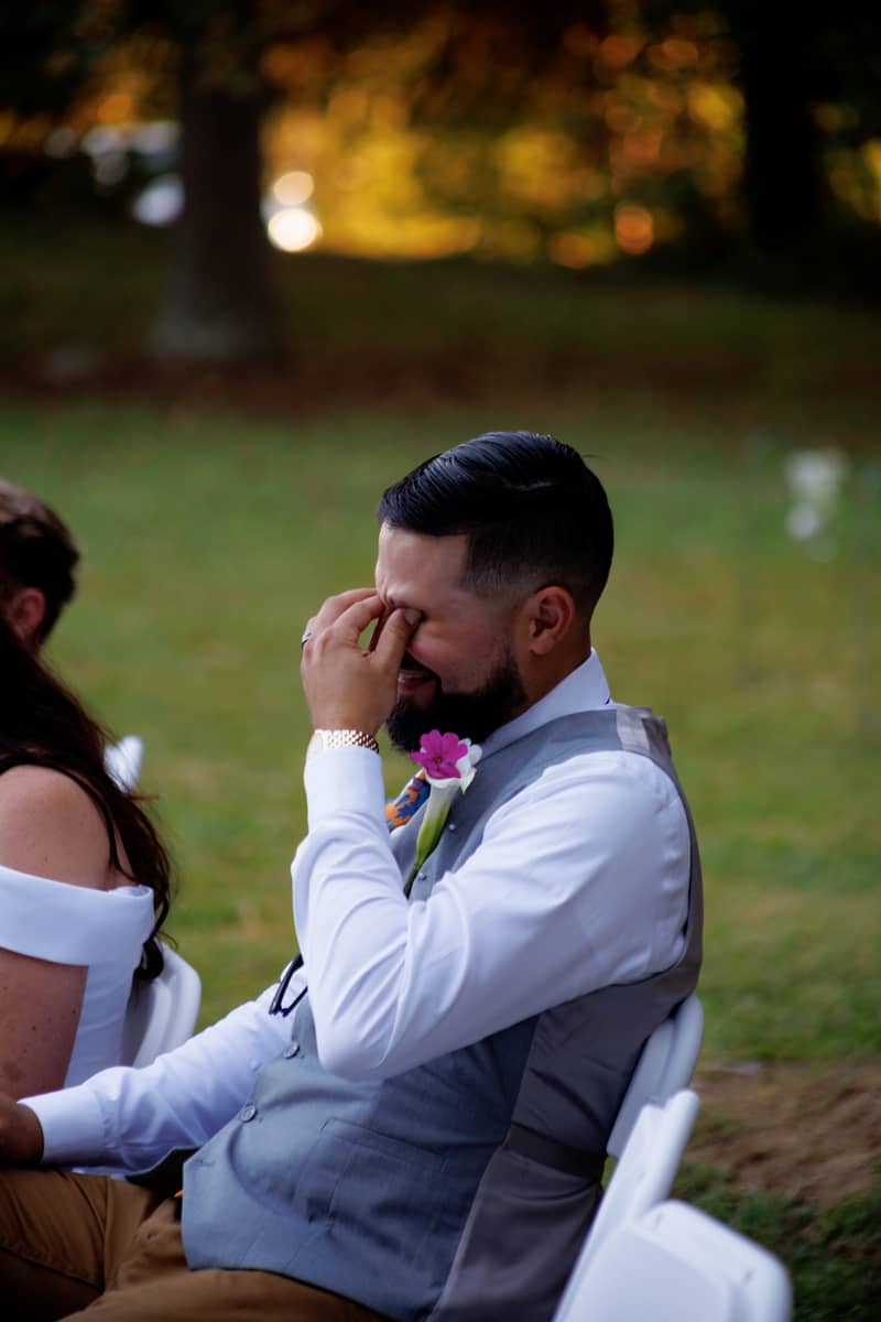 Groom wiping tears during outdoor wedding ceremony with a boutonniere