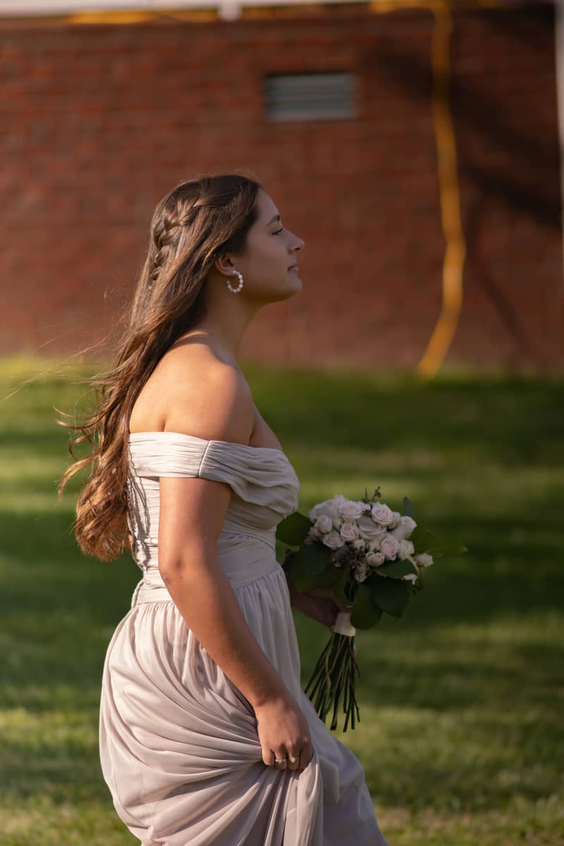 A bridesmaid in a light gown holds a bouquet while walking outdoors