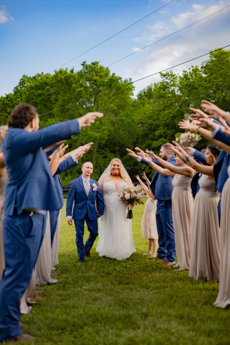 Bride and groom walk through a wedding party tunnel on a sunny day