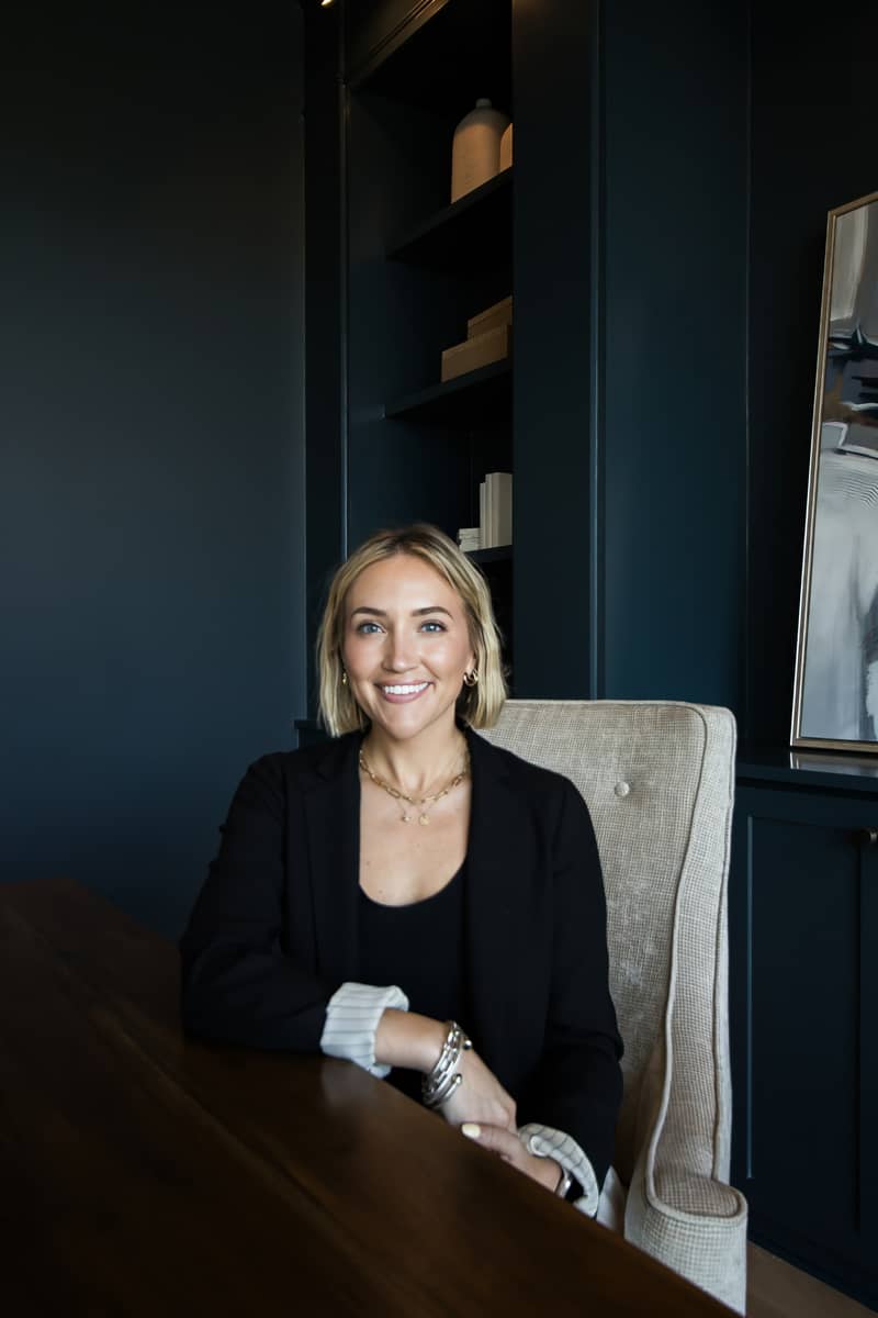 Professional headshot of a smiling woman in a black blazer sitting at a desk