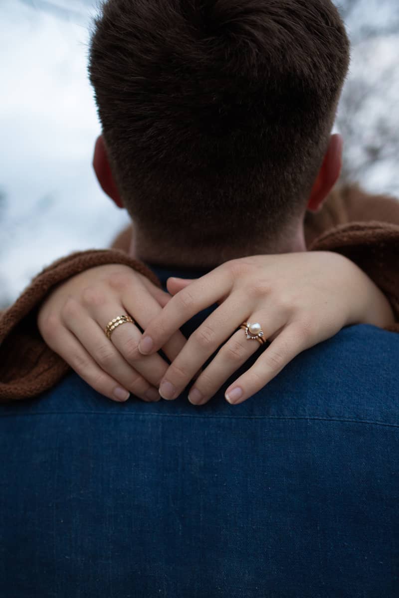Couple embracing outdoors, hands clasped showing rings, intimate and loving mood