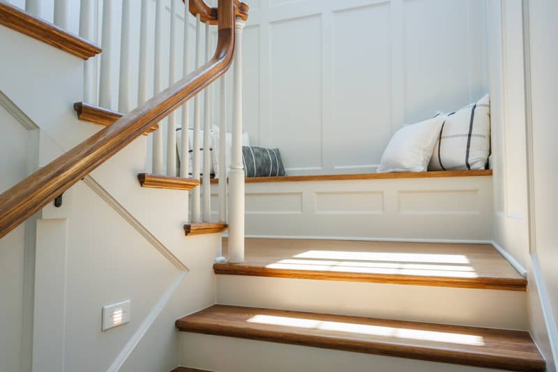 Sunlight streams across wooden stairs and a built-in bench with pillows