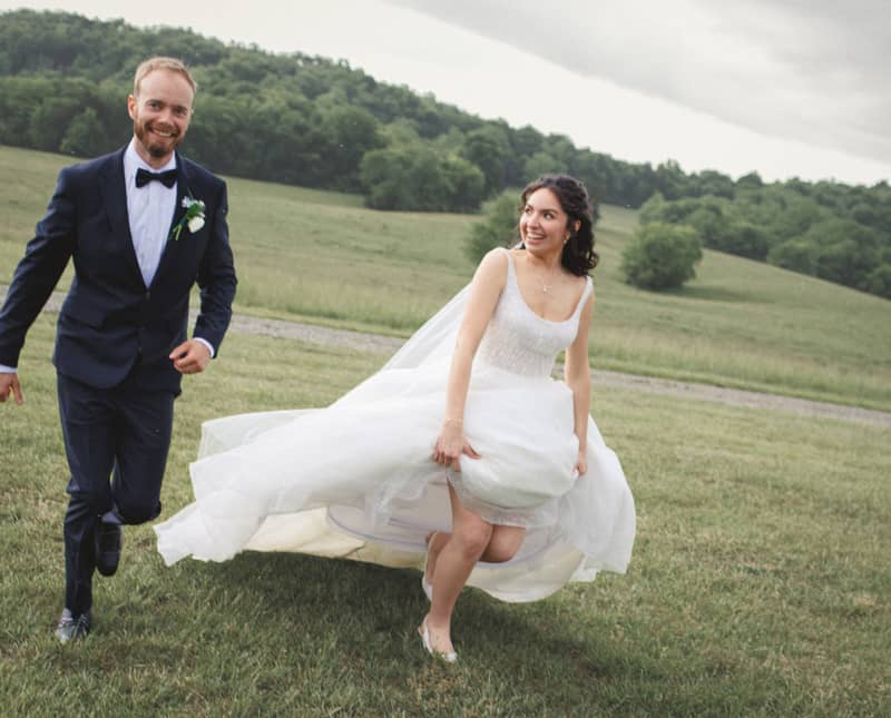 Bride and groom running happily across a grassy field on their wedding day